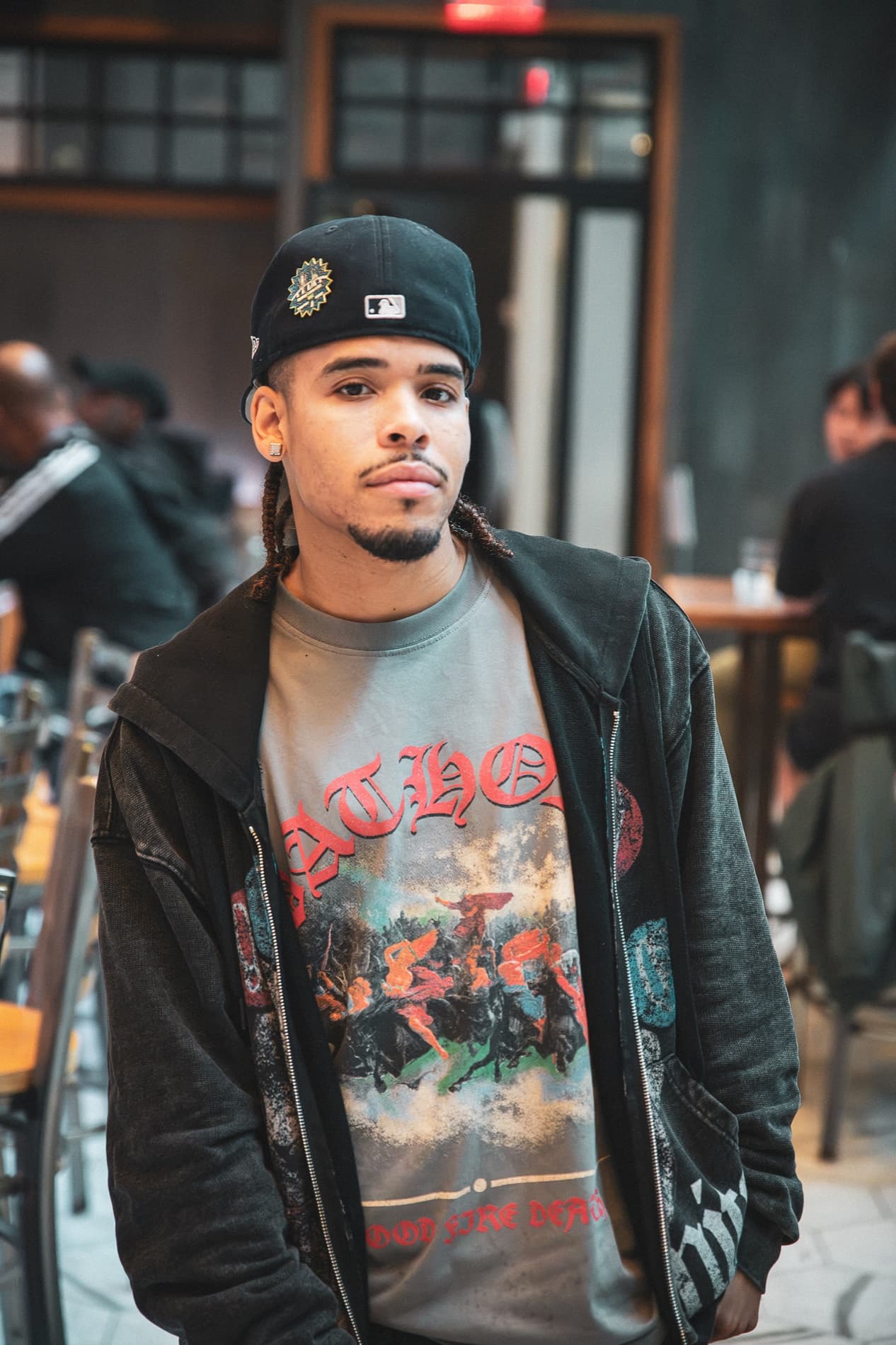 A man in a black cap and a dark hoodie poses over a graphic T-shirt in the dining room.